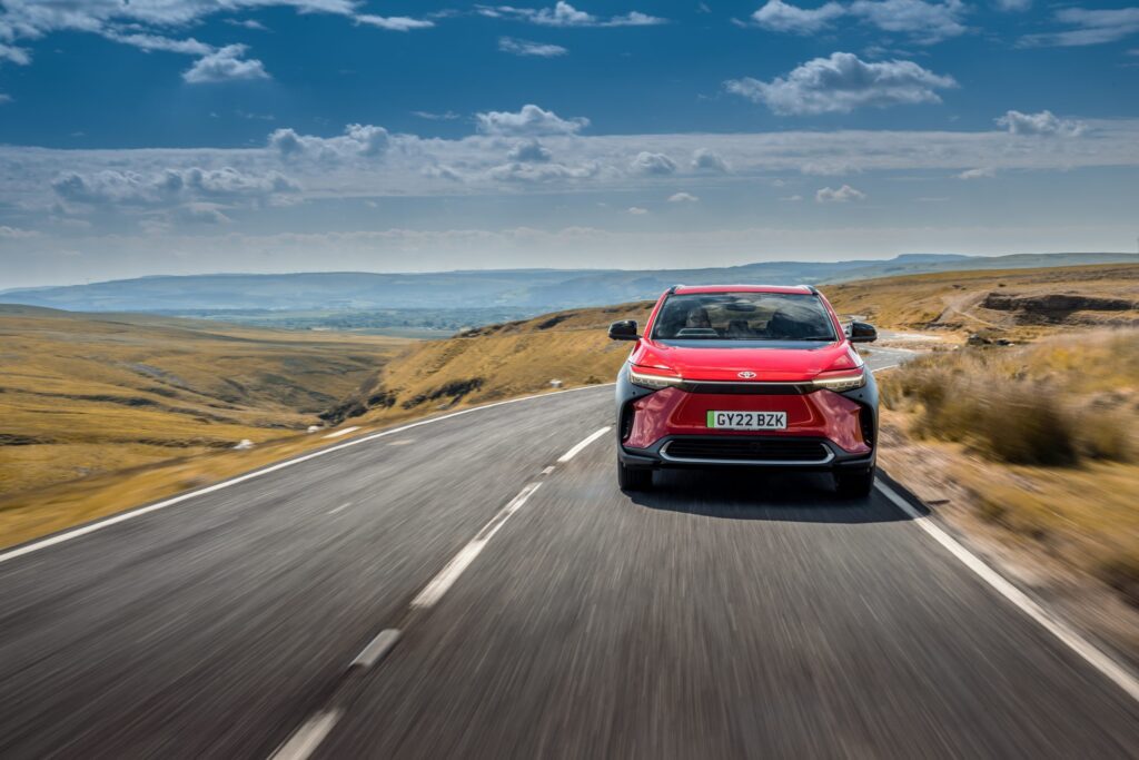 A red Toyota BZ4x driving along an empty country road in the hills